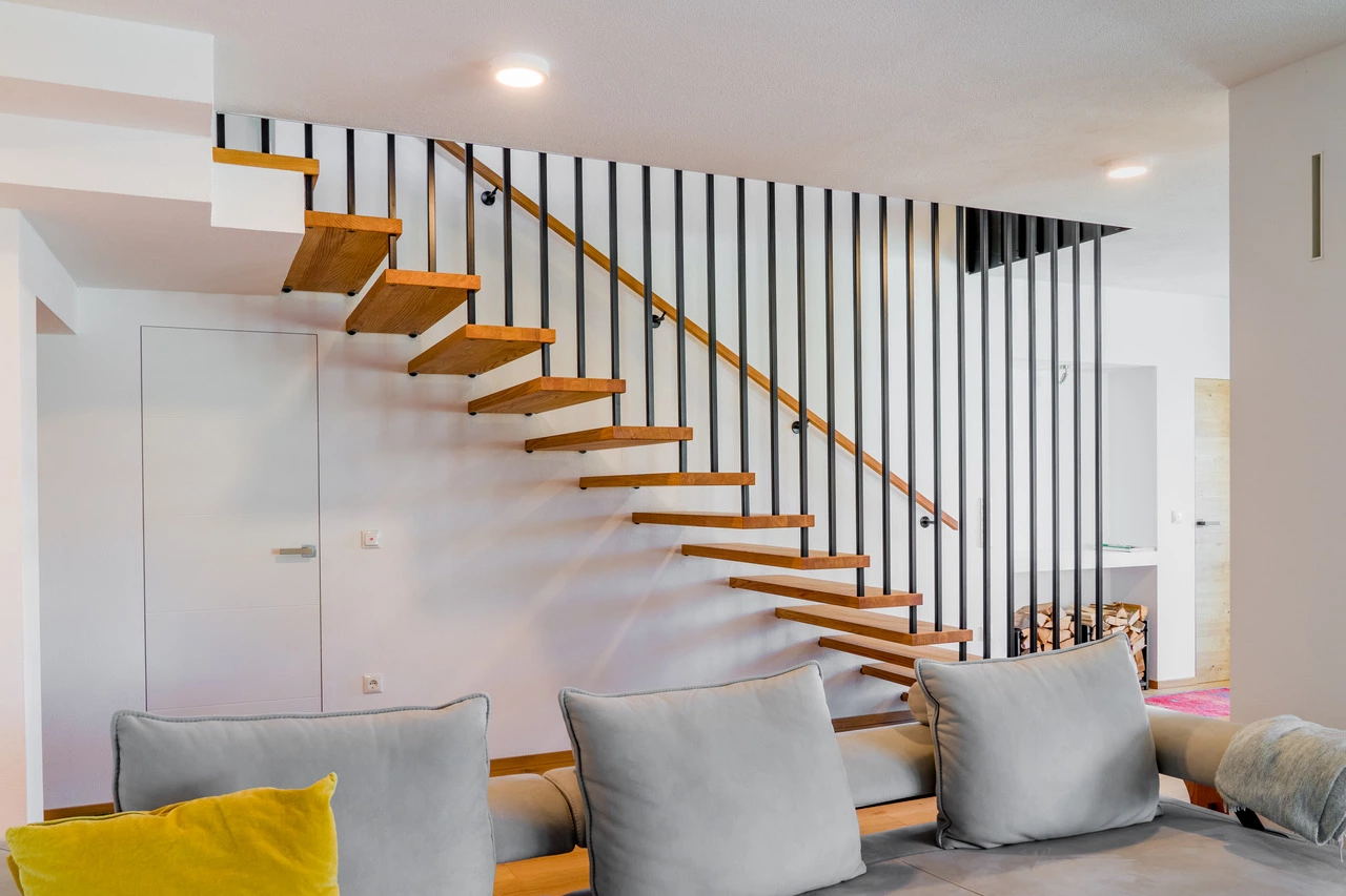 Wohnzimmer im Vordergrund eine graue Couch und im Hintergrund eine Bolzenstiege aus Eiche