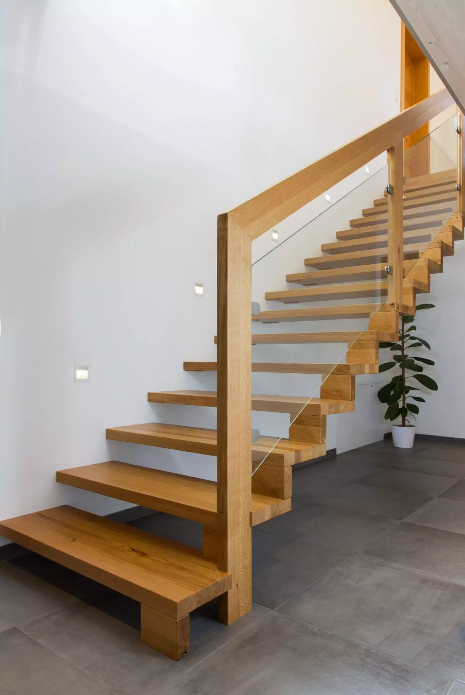 Stiegenaufgang mit Fliesenboden und einer Holztreppe im Hintergrund befindet sich eine Pflanze