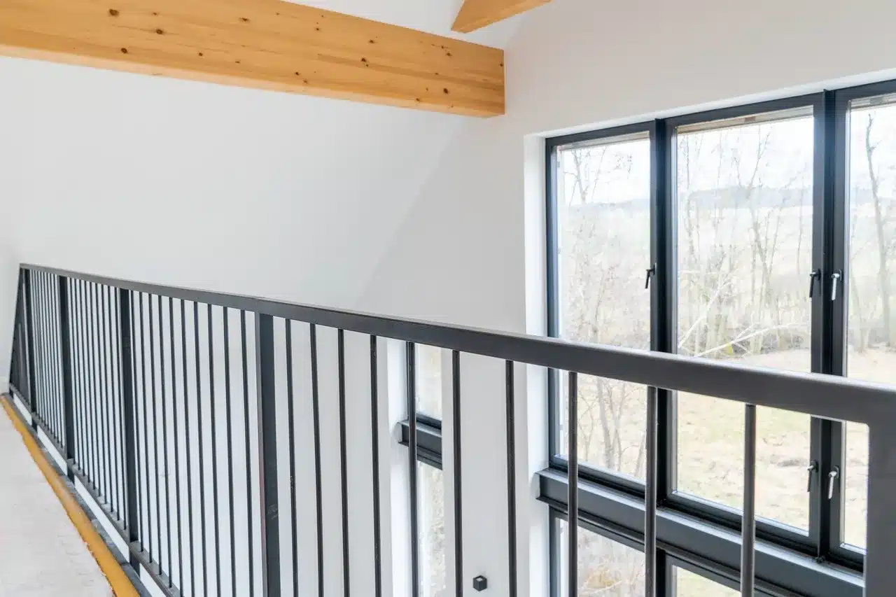 Blick auf ein schwarzes Stahlgeländer, die Decke ist weiß mit einem Holztram und einem großen Fenster im Hintergrund